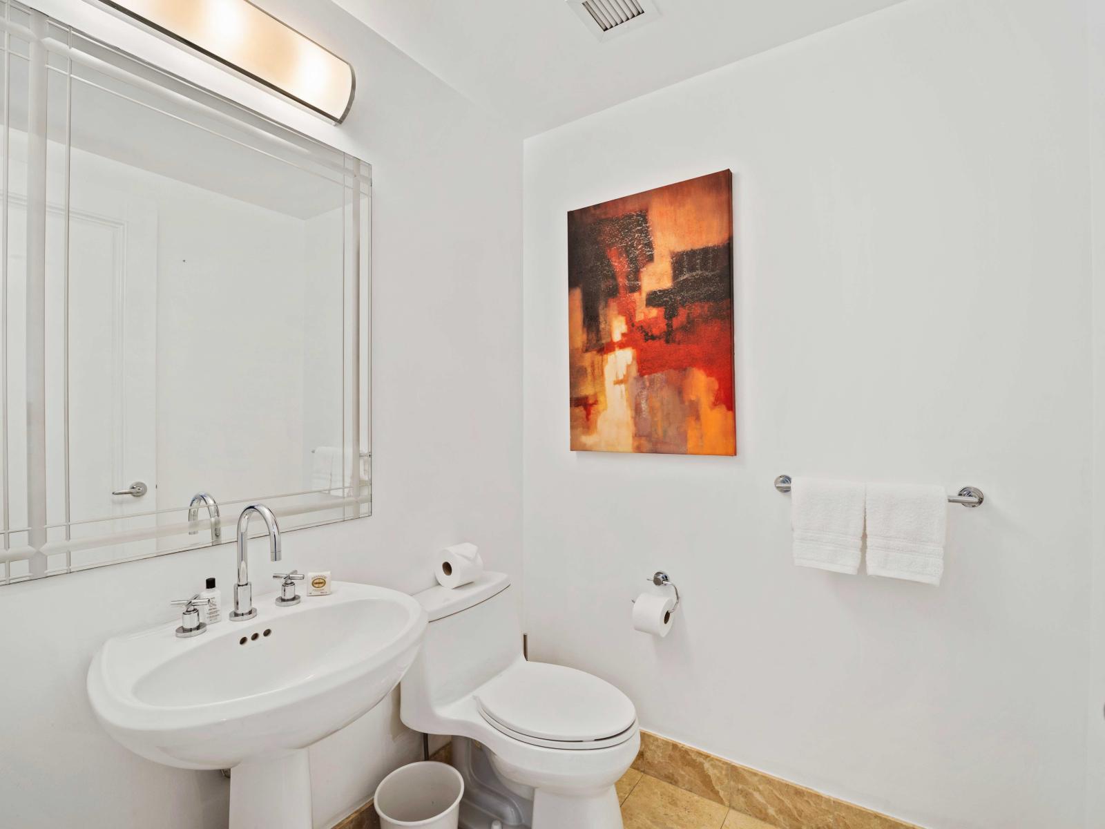 - Modern half-bathroom with a sleek pedestal sink and contemporary fixtures - Bright and clean design featuring a large mirror and stylish artwork - Well-appointed with essential amenities, providing a convenient and comfortable space