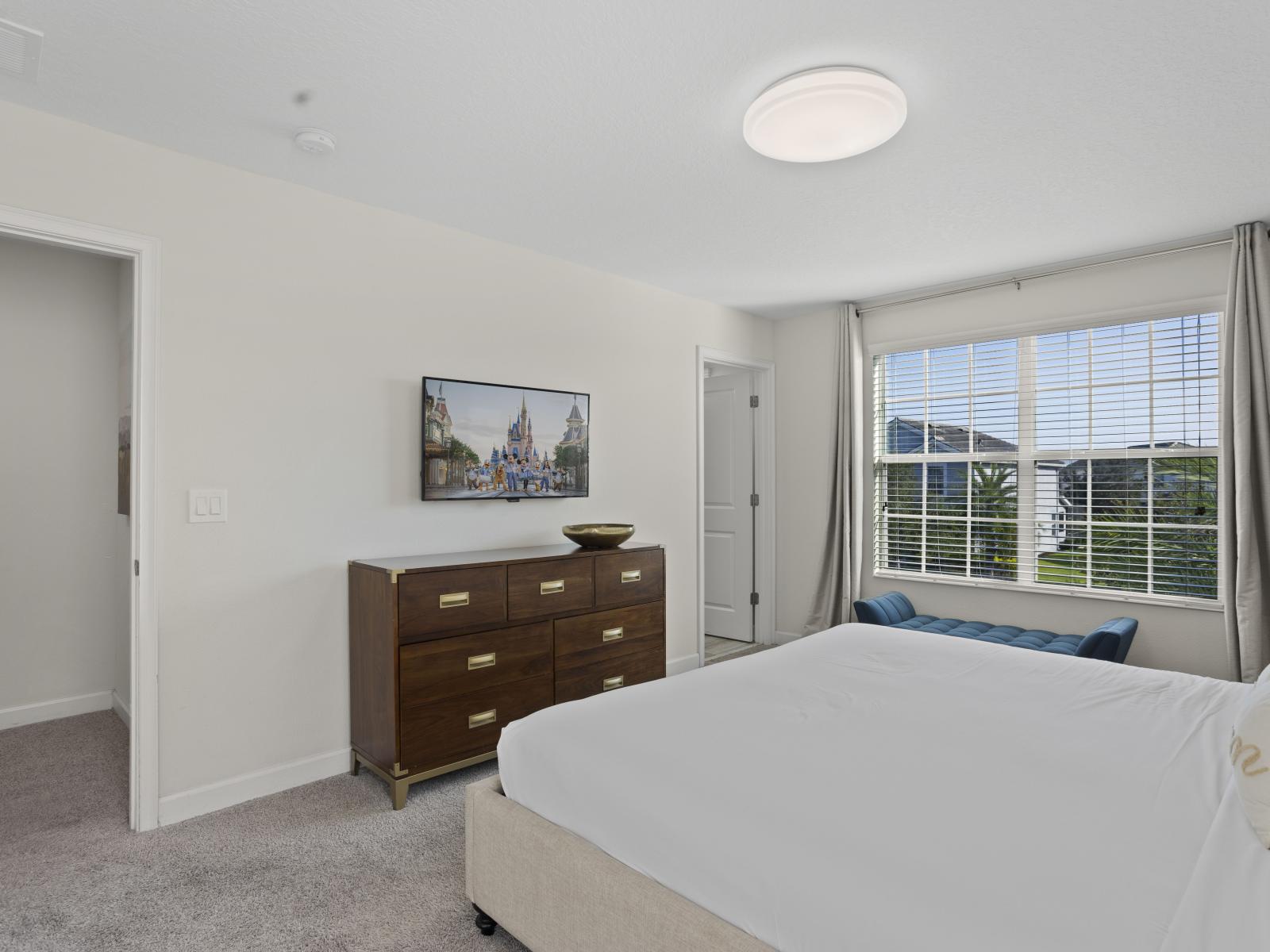 - Unwind in this bright bedroom with a large window offering scenic views - Elegant dresser and wall-mounted TV for convenience and entertainment - Comfortable and serene ambiance, perfect for relaxation after a long day