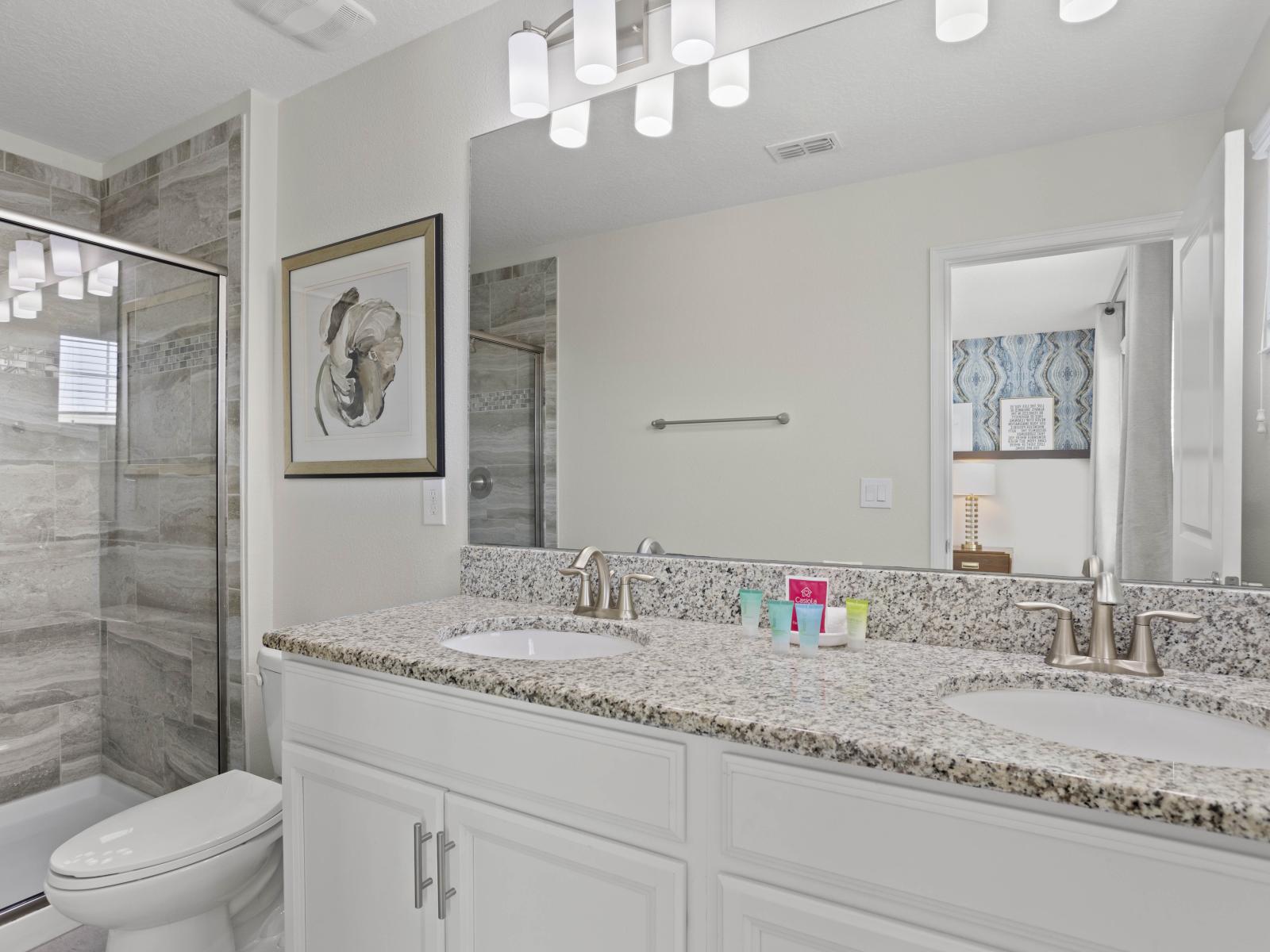 - Modern bathroom featuring a sleek double vanity with granite countertops - Large mirror and elegant lighting create a bright and spacious feel - Walk-in glass shower with contemporary tiling for a comfy experience