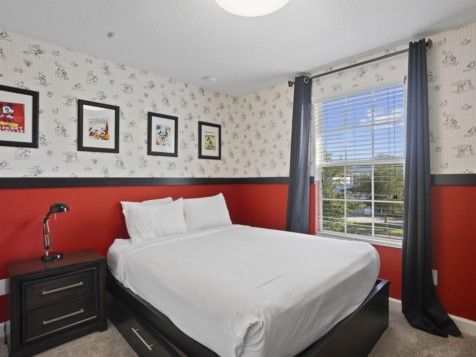 - Charming bedroom with a bold red accent wall and Disney-themed decor - Cozy bed with crisp white linens, perfect for a restful night’s sleep - Bright natural light complements the playful design and framed Mickey artwork