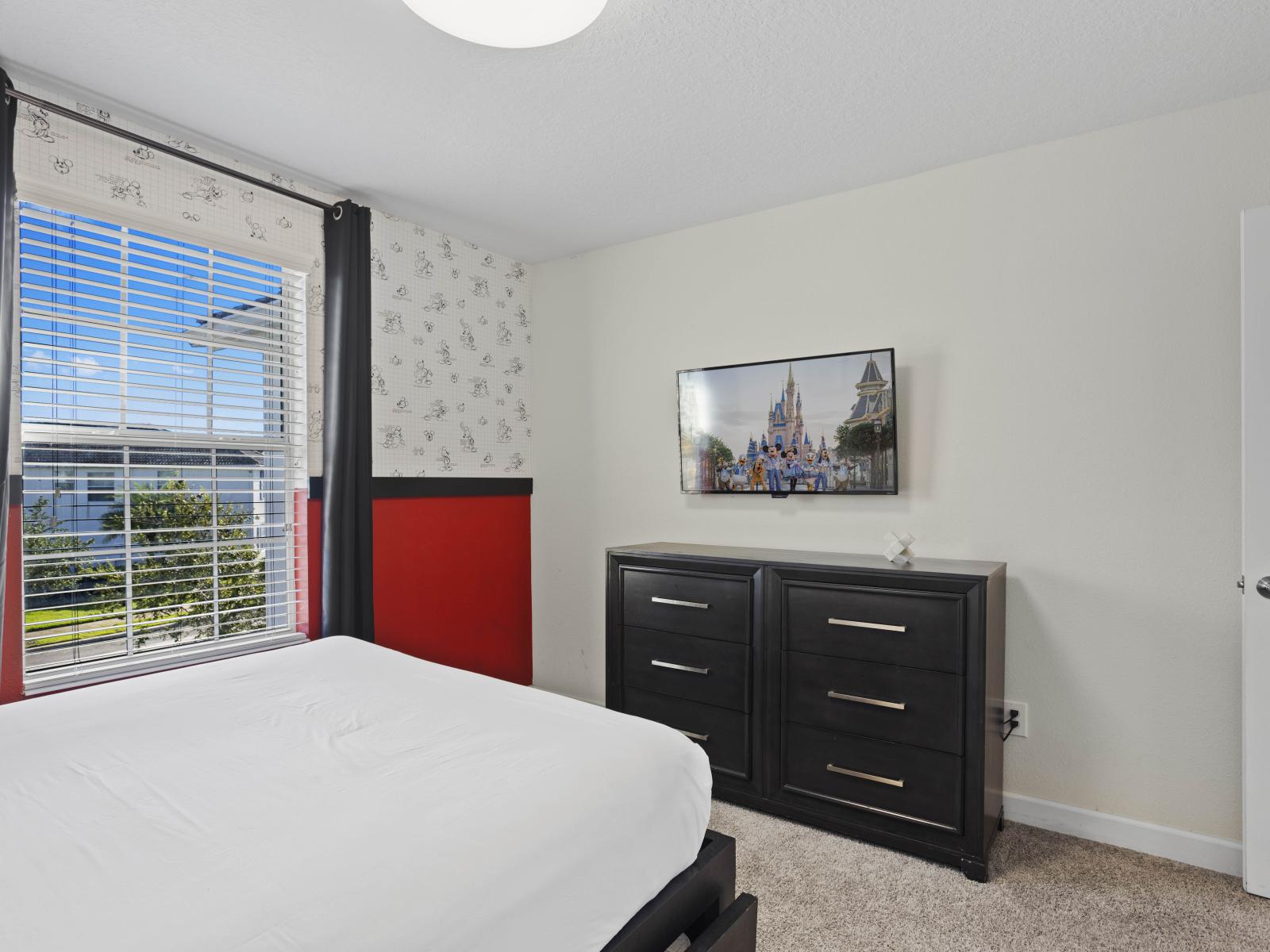 - Mickey-themed bedroom with plenty of storage provided by a modern black dresser - Wall-mounted TV adds a touch of convenience for entertainment - Vibrant colors and natural light create a cheerful, welcoming space