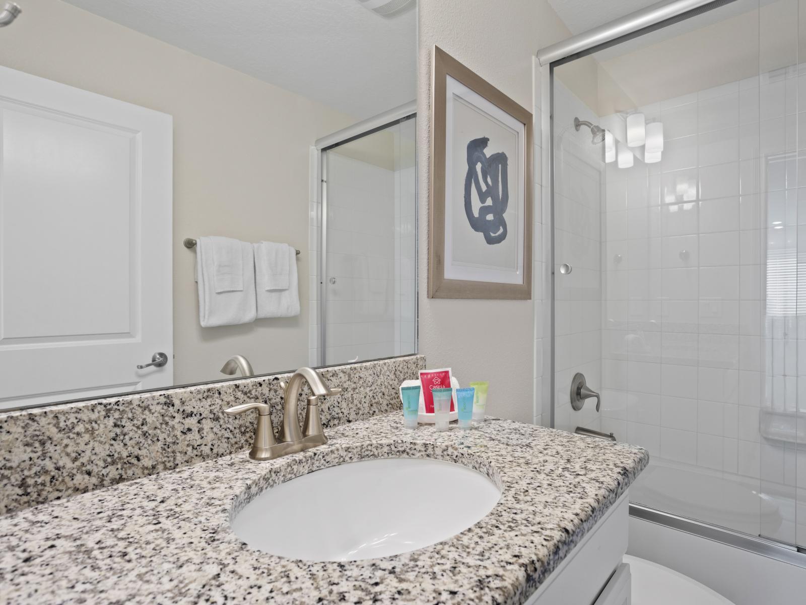 - Elegant bathroom featuring granite countertop and contemporary fixtures - Glass enclosed walk-in shower with clean, minimalist design - Well-lit vanity area for a bright and fresh look