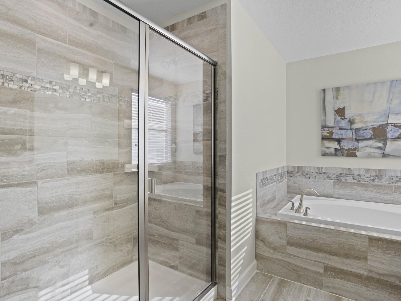 - A bathroom featuring a glass walk-in shower with modern tile design - Large bath tub for ultimate relaxation, accented with elegant stonework - Bright and serene, perfect for unwinding in a spa-like atmosphere