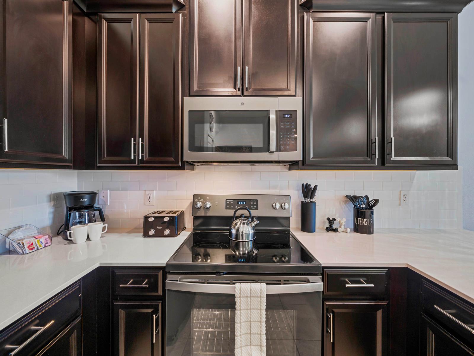 - Modern kitchen with sleek dark cabinetry and appliances for a contemporary feel - Equipped with a microwave, stove, and a coffee maker, providing everything needed for easy meal prep - Clean, bright countertops and backsplash create a polished look