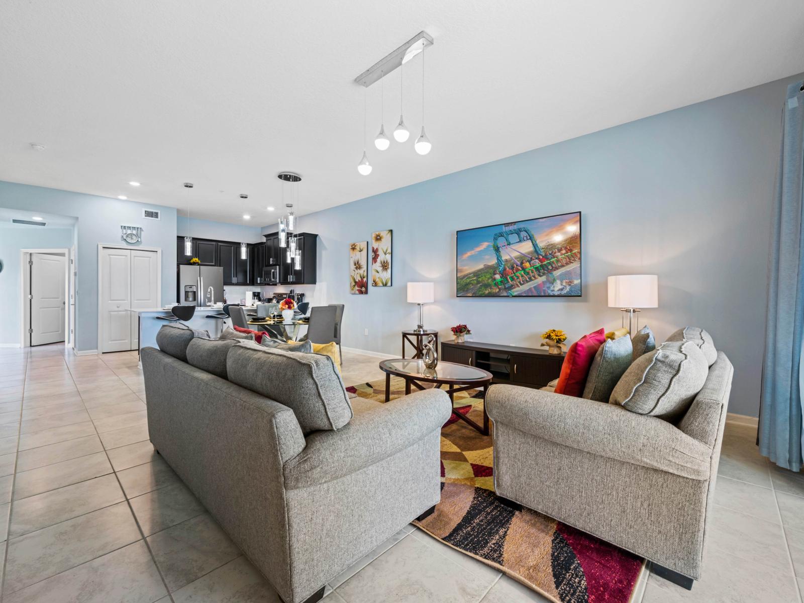 - Spacious open-concept living room with cozy seating and vibrant accent pillows - Seamless flow between the kitchen, dining, and living area, ideal for relaxing or entertaining - Large flat-screen TV and natural light create a bright, inviting space