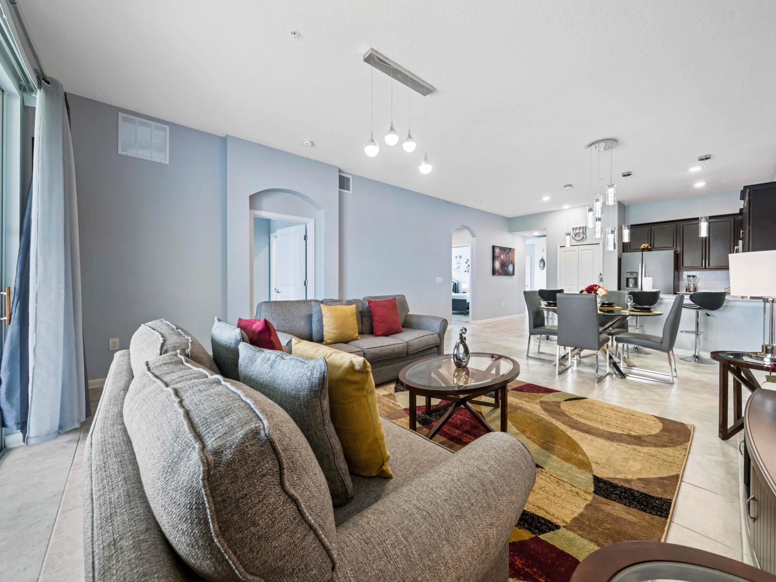 - Bright and airy living room with plush seating and vibrant accent pillows - Seamless flow from the living area to the kitchen and dining, perfect for entertaining - Large sliding doors bring in natural light and open to a scenic outdoor space