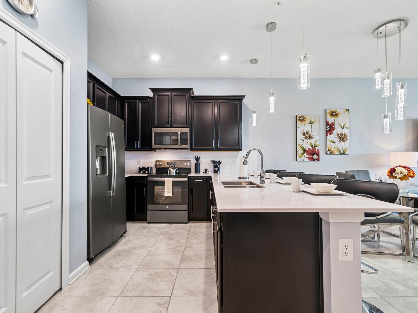 - Modern kitchen with black cabinets and stainless steel appliances for a sleek, stylish look - Large island with built-in sink offers extra counter space and casual dining - Elegant pendant lights add a contemporary touch to the open layout