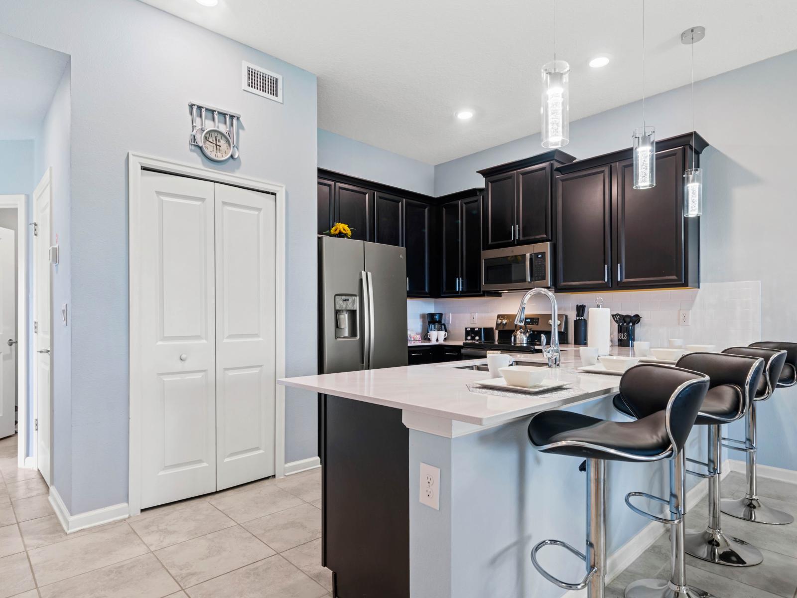 - Modern kitchen island with seating for four, featuring sleek black stools for casual dining or socializing - Stainless steel appliances and dark cabinetry create a contemporary atmosphere - Pendant lighting adds an elegant touch to the space