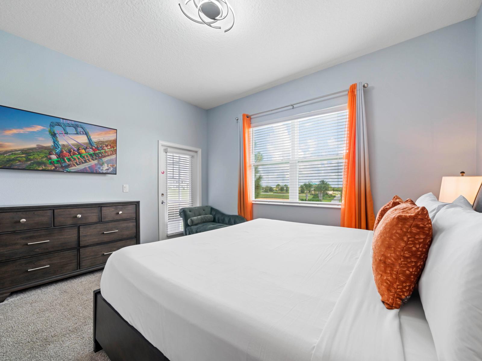 - King-size bed complemented by soft orange accent pillows and bedside lamps - Includes a flat-screen TV mounted above a spacious dresser with plenty of storage space - Features large windows with bright curtains and access to a private outdoor area