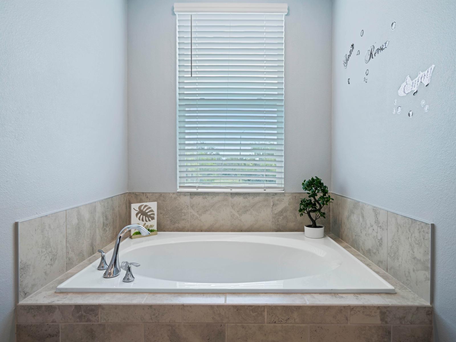 - Spacious soaking tub set against a tiled backdrop, perfect for relaxation   - Window allowing natural light to flow in, creating a serene ambiance   - Elegant chrome fixtures add a touch of modern sophistication, creating a peaceful atmosphere