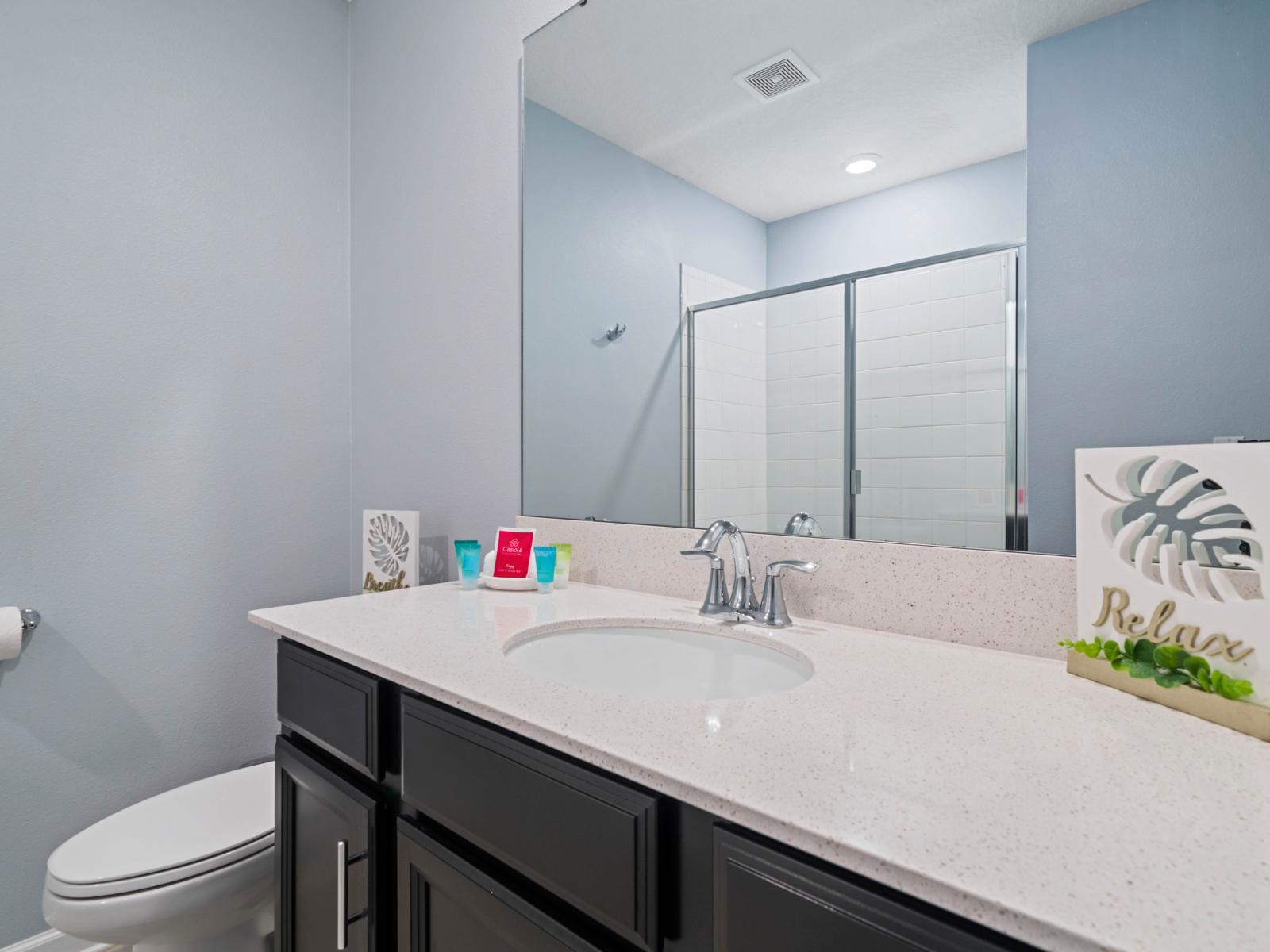 - Bathroom features a large vanity with a sleek, polished countertop and modern fixtures - A spacious walk-in shower with clear glass doors and white tile design offers a refreshing experience - Minimalist décor with calming and relax accents