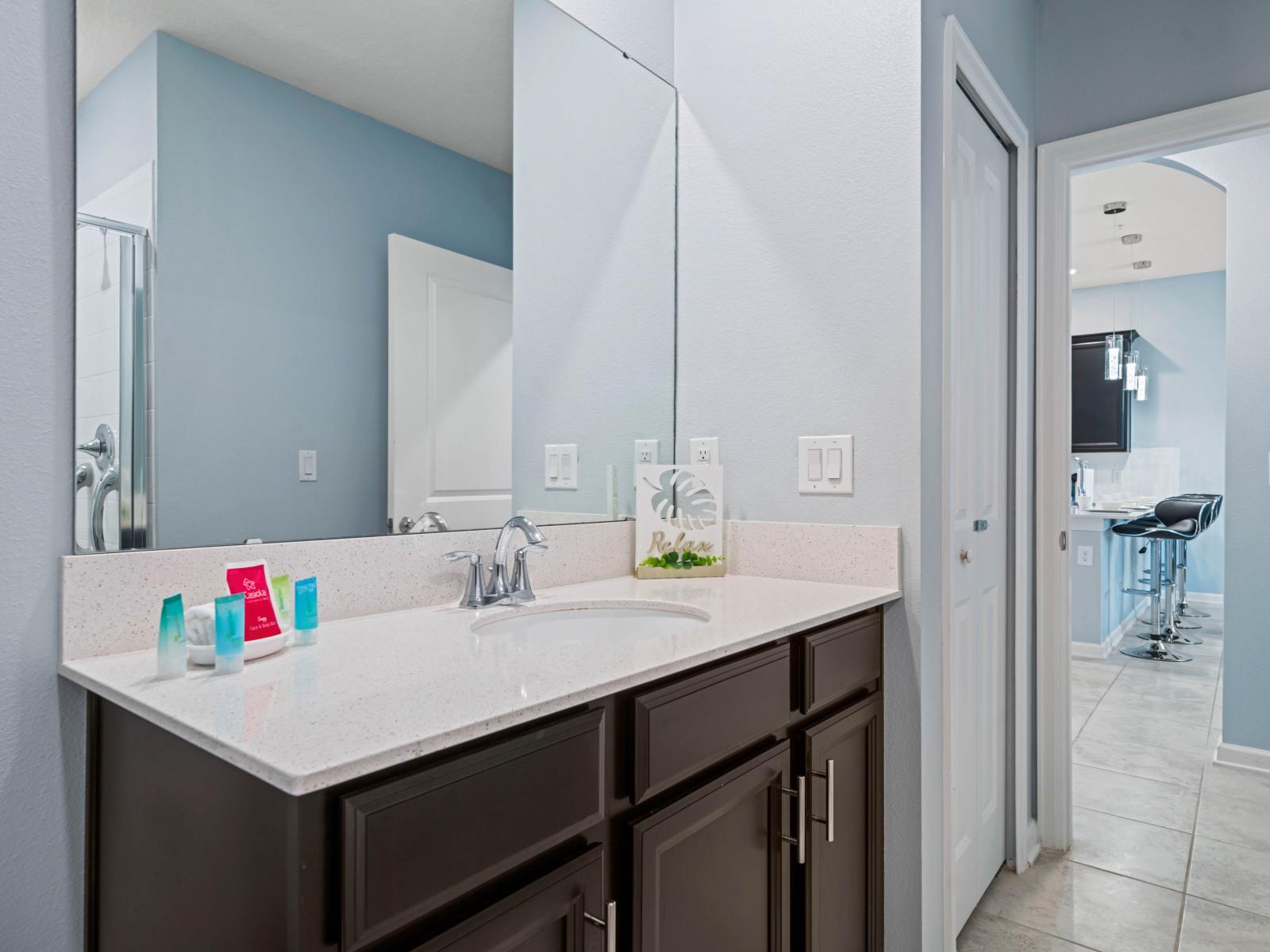 - Stylish bathroom with a modern vanity and a large mirror, offering space for essentials - A sleek, white countertop and chrome fixtures elevate the bathroom’s elegant appeal - Convenient access to the living area for a seamless flow between spaces