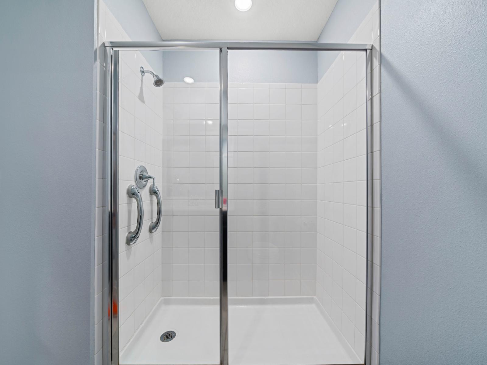 - Spacious walk-in shower featuring sleek glass doors for a modern, minimalist look - Polished chrome fixtures add a touch of elegance to the bright, white-tiled interior - Easy-to-use handle bars for added comfort and convenience during use