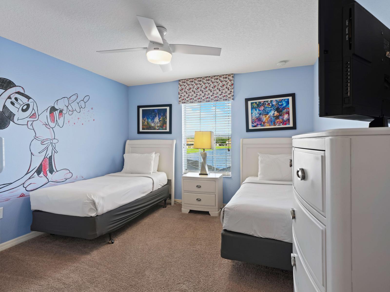 - Fun and playful bedroom with a light blue theme, featuring twin beds and a large mural of Mickey Mouse on the wall - Natural light from the window, overlooking a scenic view - Room is equipped with a TV, perfect for relaxing and entertainment