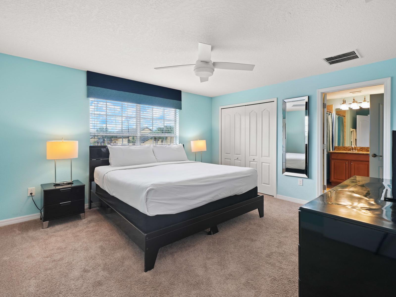 - Vibrant bedroom featuring a bed with crisp white linens and a striking turquoise accent wall - Black nightstands and matching lamps enhance the contemporary feel - Window bring in natural light, highlighting the cozy carpet and spacious layout