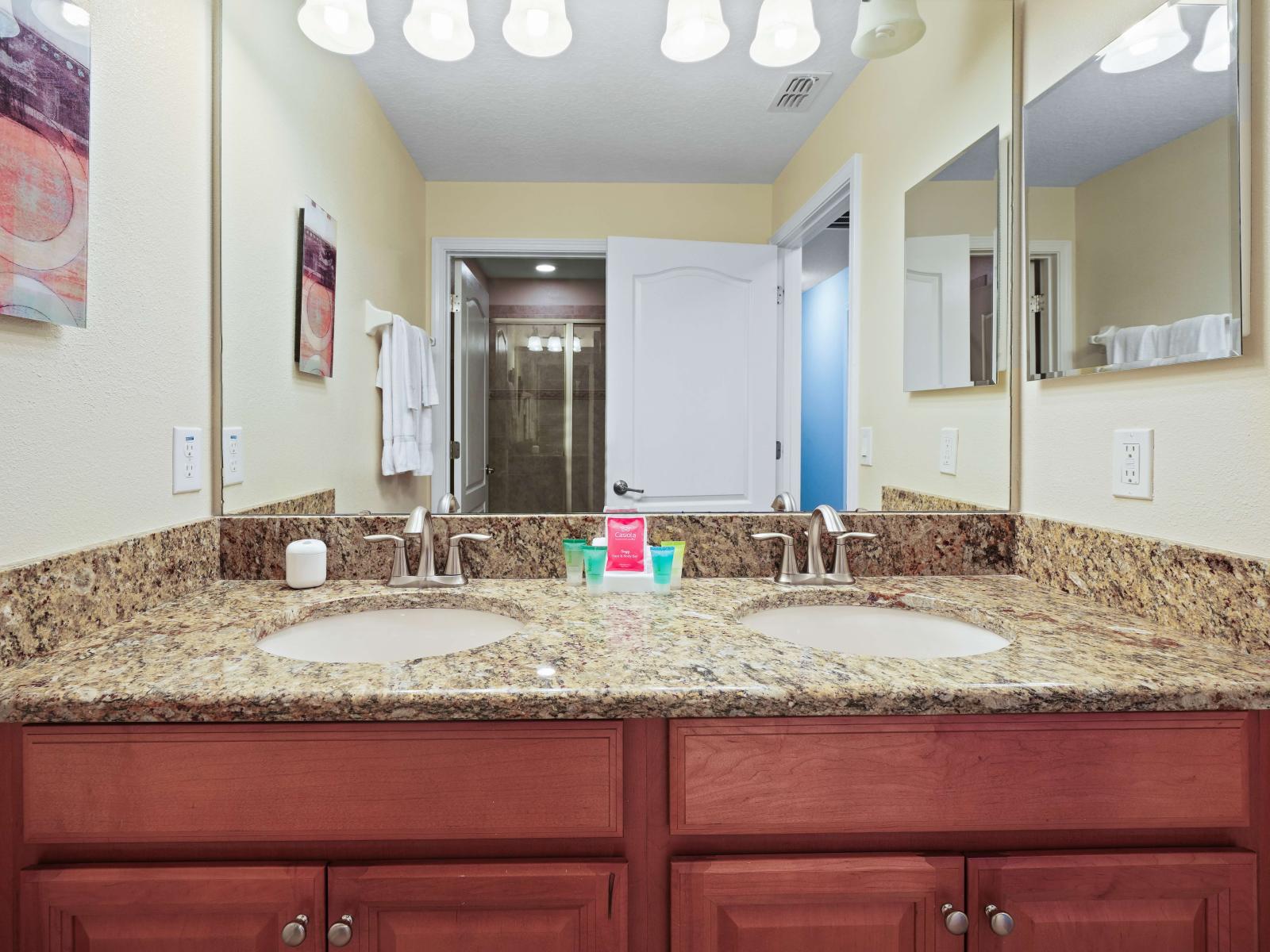 - Elegant bathroom with a double sink vanity featuring granite countertops and warm wood cabinetry - Soft lighting and mirror enhance the spacious feel - Neutral wall tones create a calming atmosphere, complementing the functional and stylish design