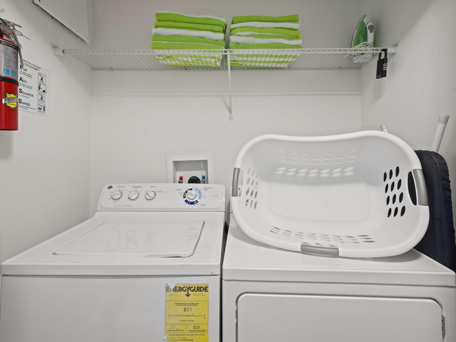 - Compact laundry room with a washer and dryer, neatly organized for convenience - Shelving above holds folded green towels and laundry essentials - Laundry basket, ironing board complete the functional setup for everyday needs for the perfect stay