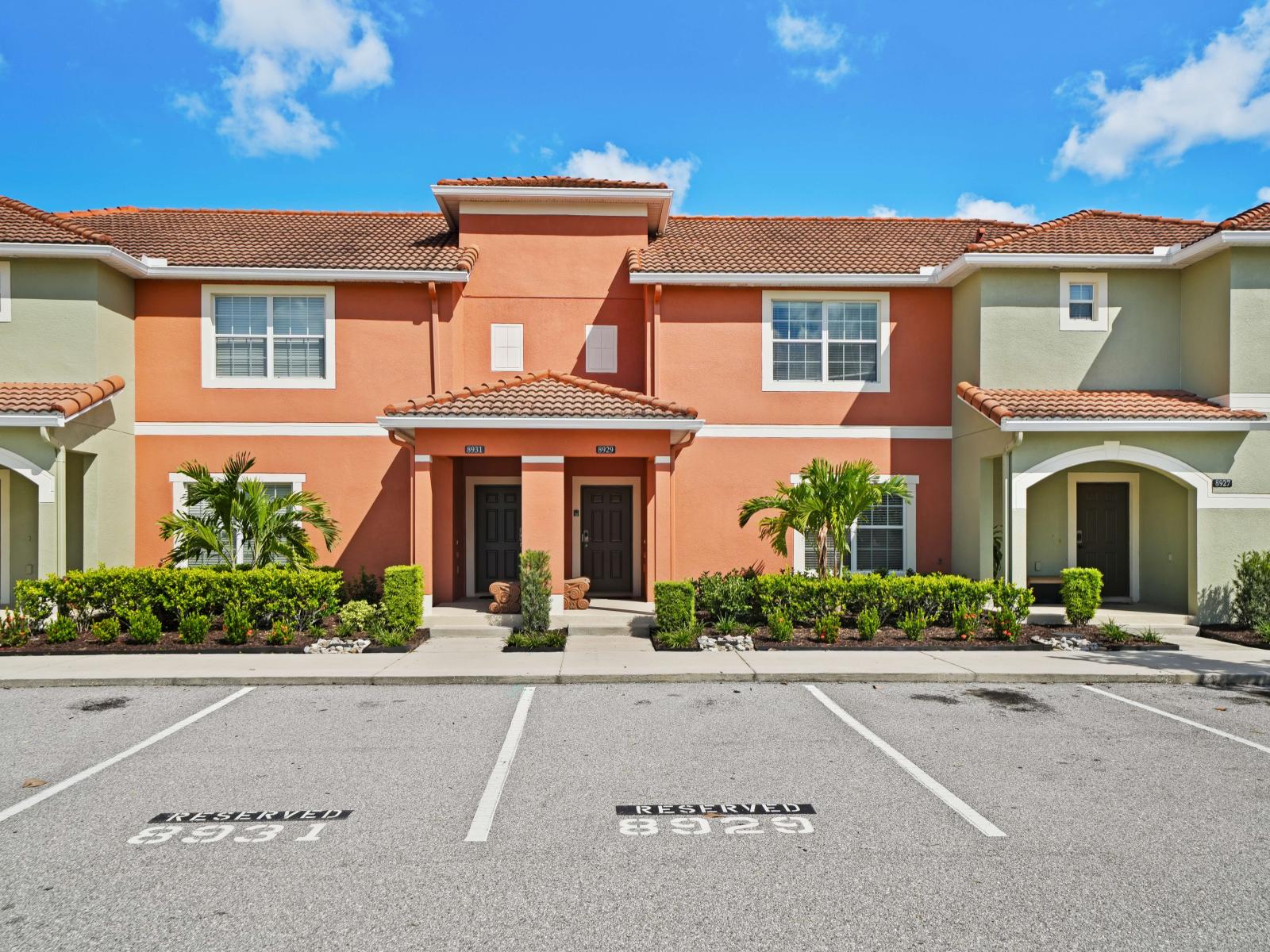 Charming townhouse exterior with vibrant orange and green accents, surrounded by lush landscaping.