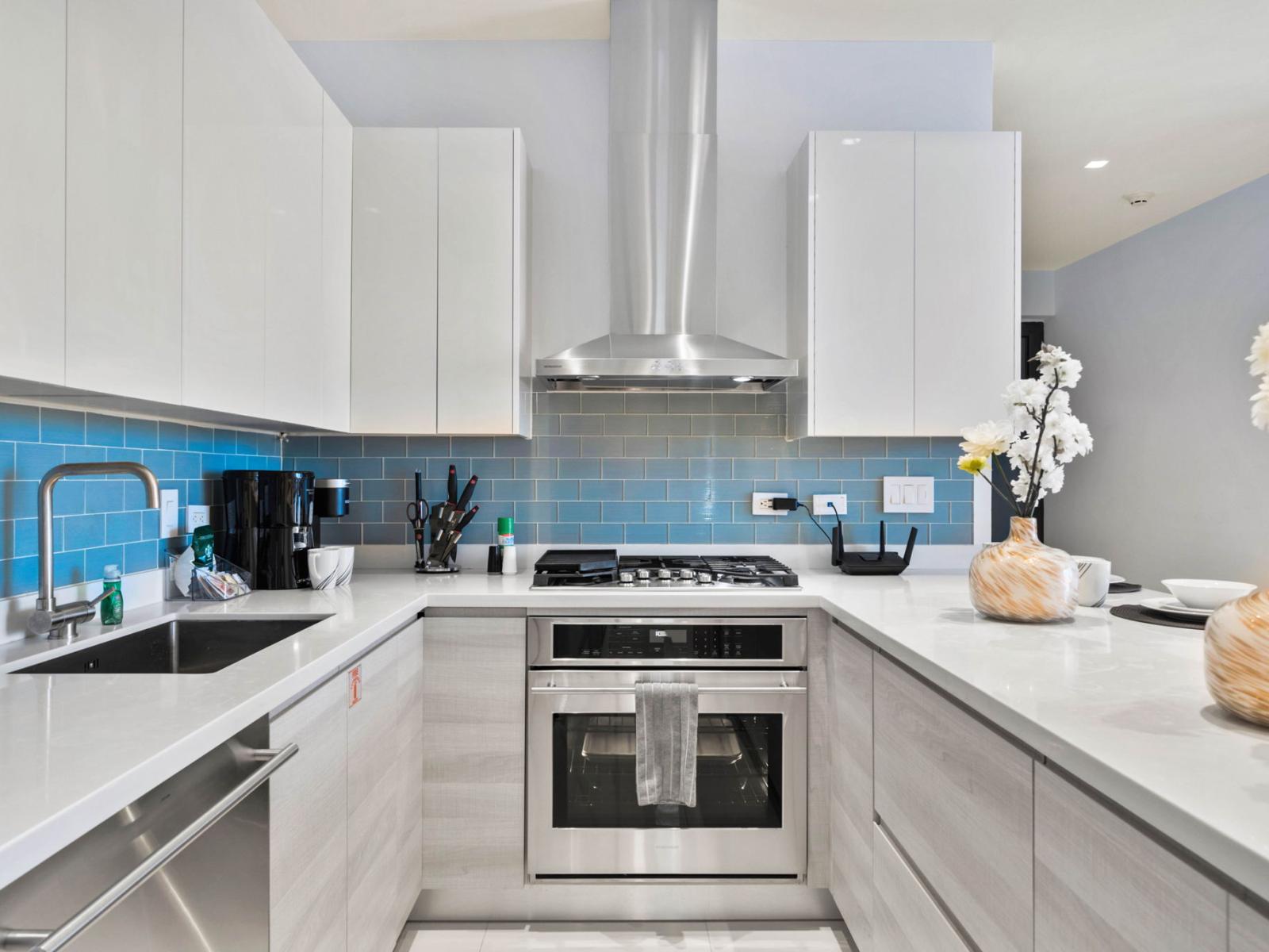 - Graceful kitchen with sleek countertops and modern appliances for meals prep - Vibrant blue backsplash adds a pop of color to the clean, white aesthetic - Plenty of counter space with all the essentials for a seamless cooking experience