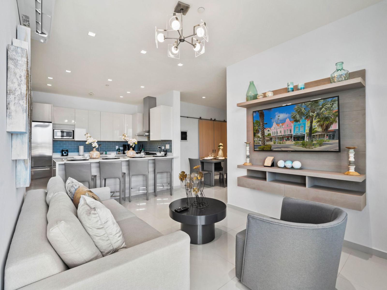 - Unwind in this charming open-plan living area with soft plush seating and elegant decor - Smart TV and sleek shelving create a perfect entertainment space - Flows seamlessly into the kitchen, making it ideal for socializing and relaxing