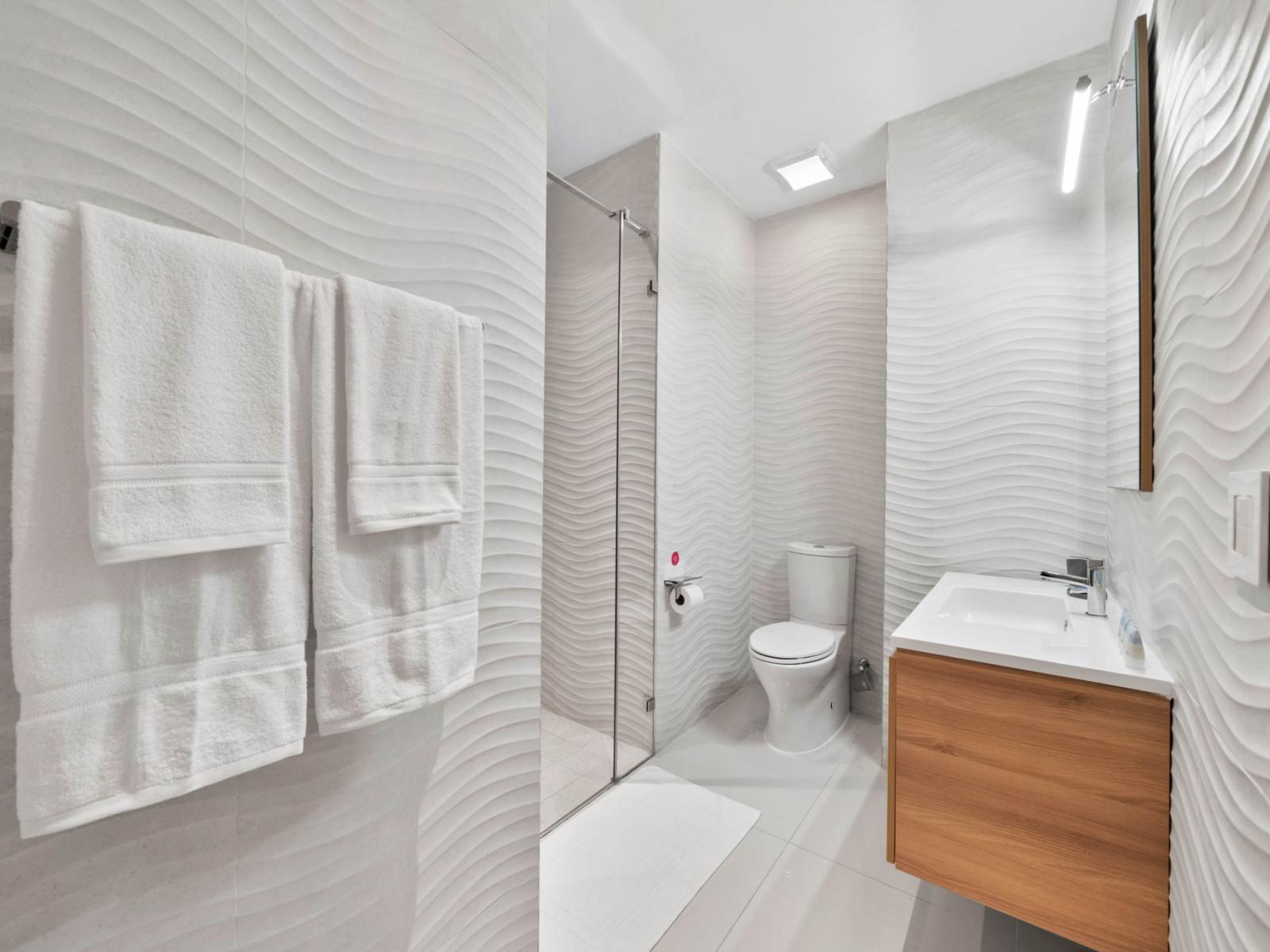 -  Relax in this contemporary bathroom with a minimalist design and textured walls - Glass enclosed  walk-in shower and plush towels offer a spa-like experience - Plenty of space with natural light, making it an ideal spot for unwinding