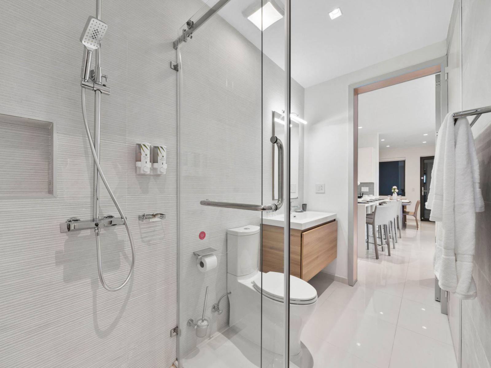 - Step inside this elegant bathroom with a glass enclosed walk-in shower and modern fixtures - Spacious design with a floating vanity and sleek lighting for a luxurious feel - Convenient access from the main living area, perfect for freshening up.