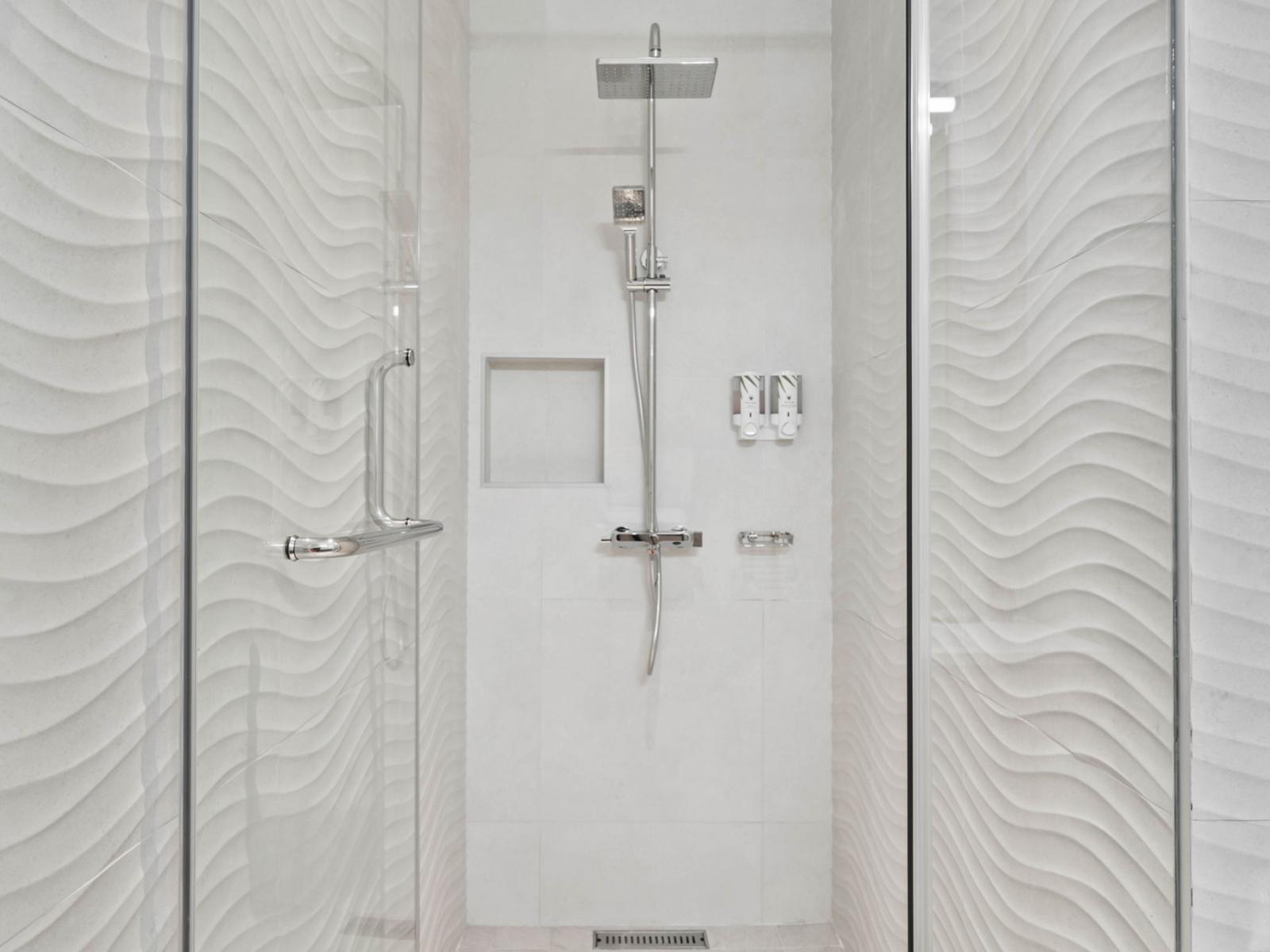 - A beautiful walk-in shower with modern fixtures and a rainfall showerhead - Textured wall design enhances the luxurious spa-like experience - A clean, open layout creates a calming and refreshing atmosphere