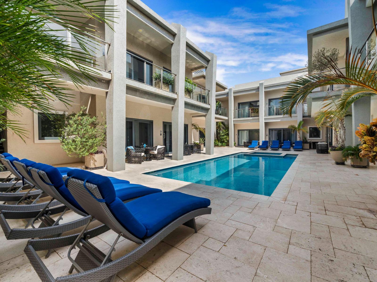 - Charming shared pool area surrounded by lounge chairs and lush greenery - Relax and soak up the sun by the pool or take a refreshing swim - A serene space for relaxation and socializing in a resort-style setting