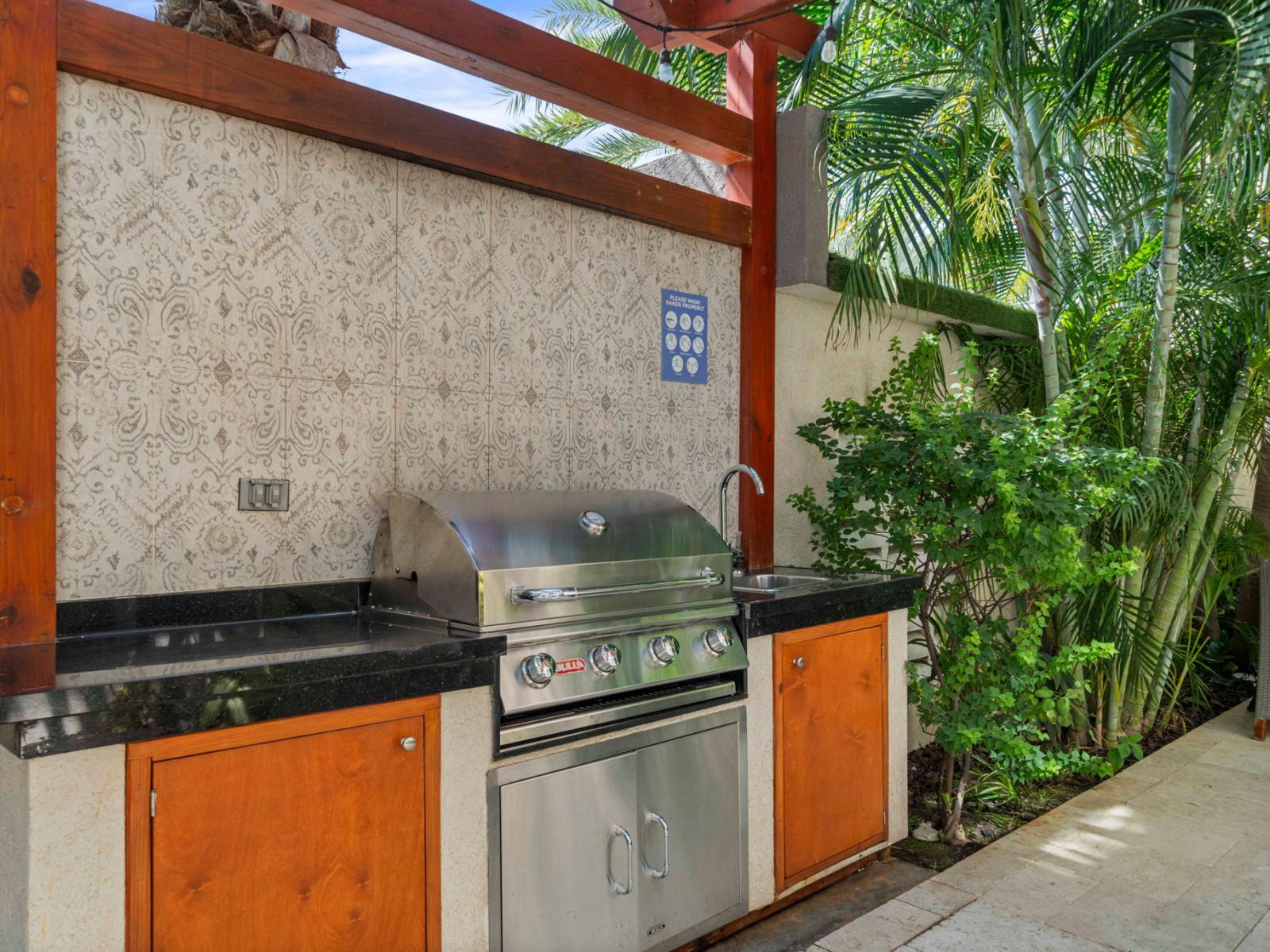 - Thoughtfully designed outdoor kitchen with a modern stainless steel grill - Stylish tile backsplash adds charm to the elegant, functional space - Nestled among tropical plants, perfect for cooking and enjoying outdoor meals