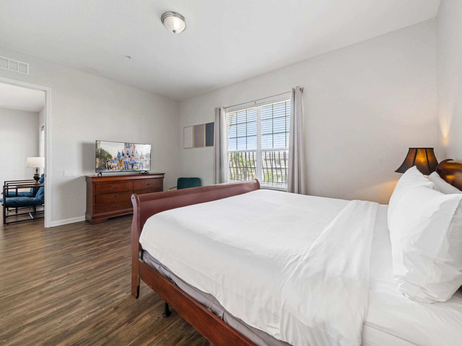 - Spacious master bedroom featuring a comfortable bed with crisp, white linens - Large windows invite natural light, while hardwood floors & tasteful decor add warmth - Includes a smart TV & a cozy seating area for your ultimate comfort & relaxation