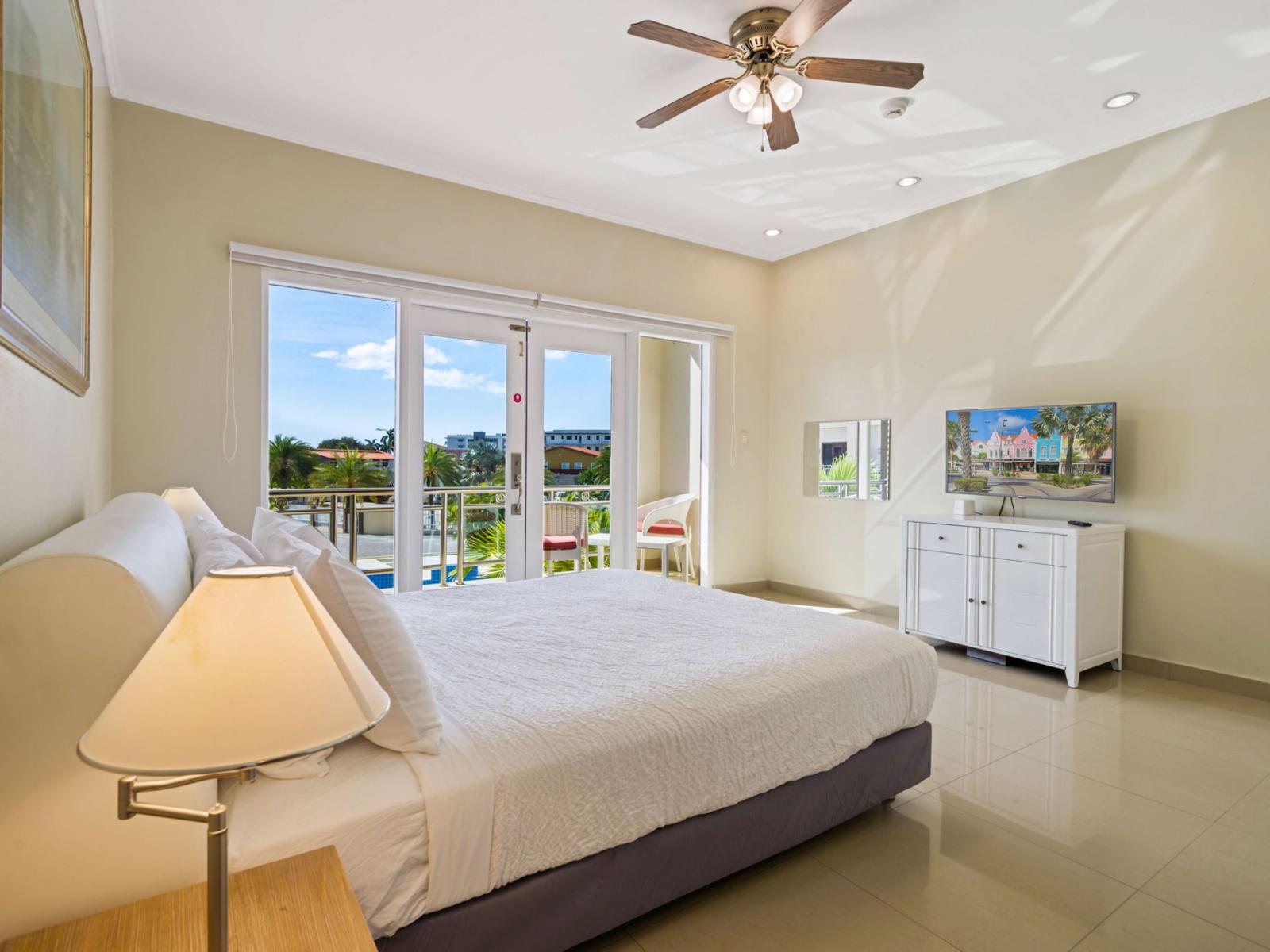 Wake up to stunning tropical views in this spacious bedroom, featuring a plush king bed, private balcony access, and a flat-screen TV for ultimate comfort and relaxation.