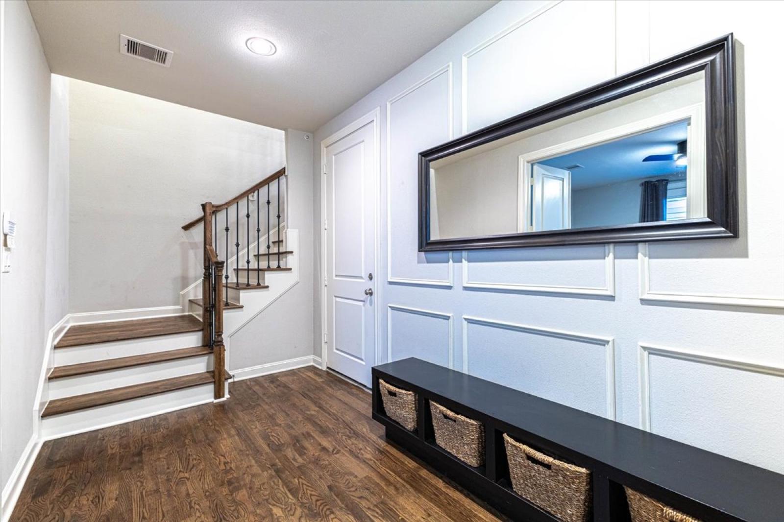 Entry foyer with hardwood floors, chic wall moldings, a bench with storage, a large mirror and staircase with wrought-iron accents complete this welcoming first impression.