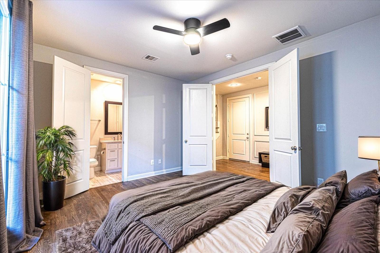 Bedroom 3 on entry level with a cozy en-suite,  modern decor, a ceiling fan, and soft lighting, local closet space & easy access to the home’s patio - perfect for comfort & convenience during your stay!