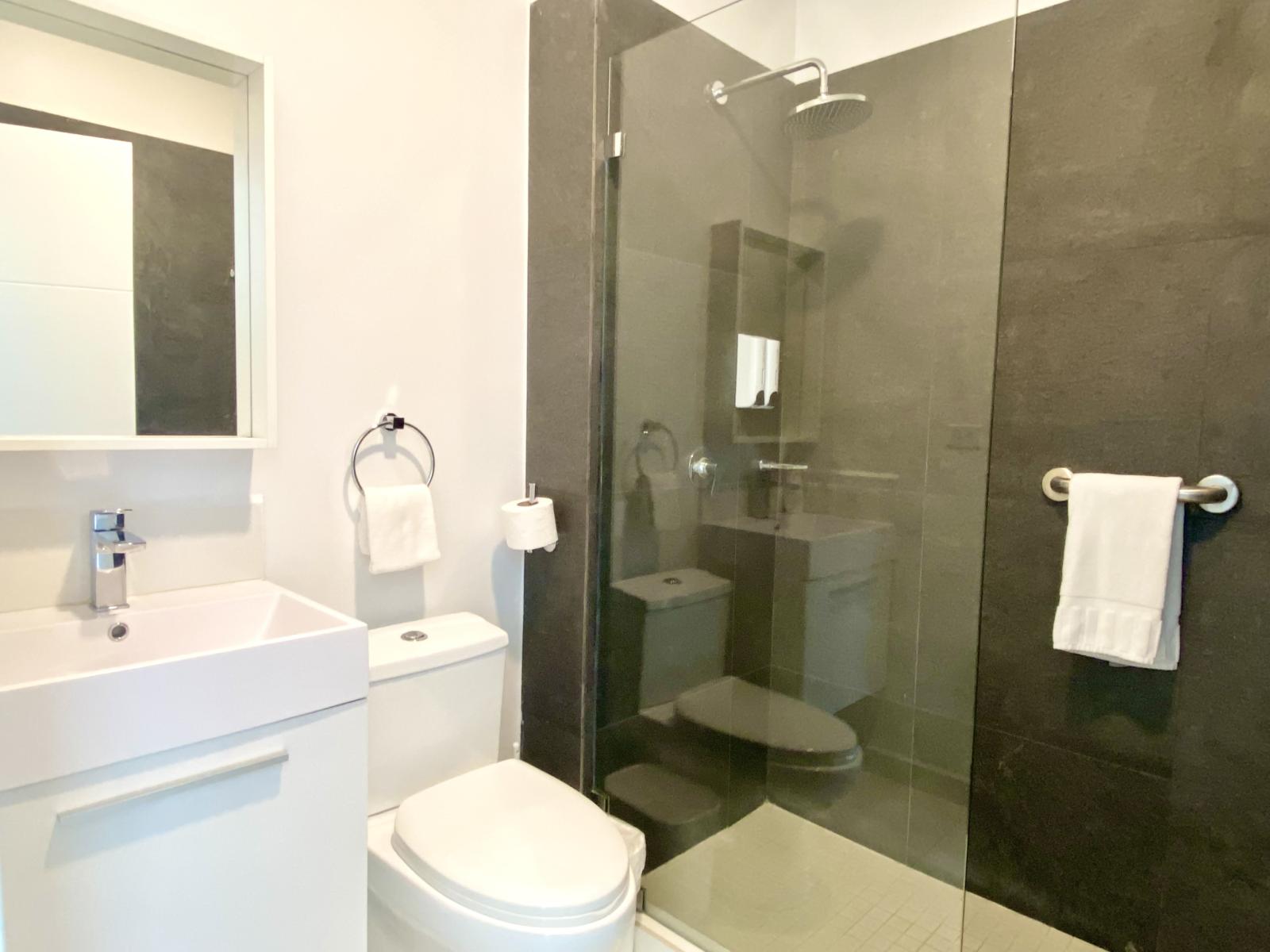 Modern bathroom featuring a walk in rainfall shower with dark stone tiles - Contemporary space with fresh towels & all the essentials for a refreshing stay - Designed for comfort & style, offering a spa like shower experience in an elegant setting