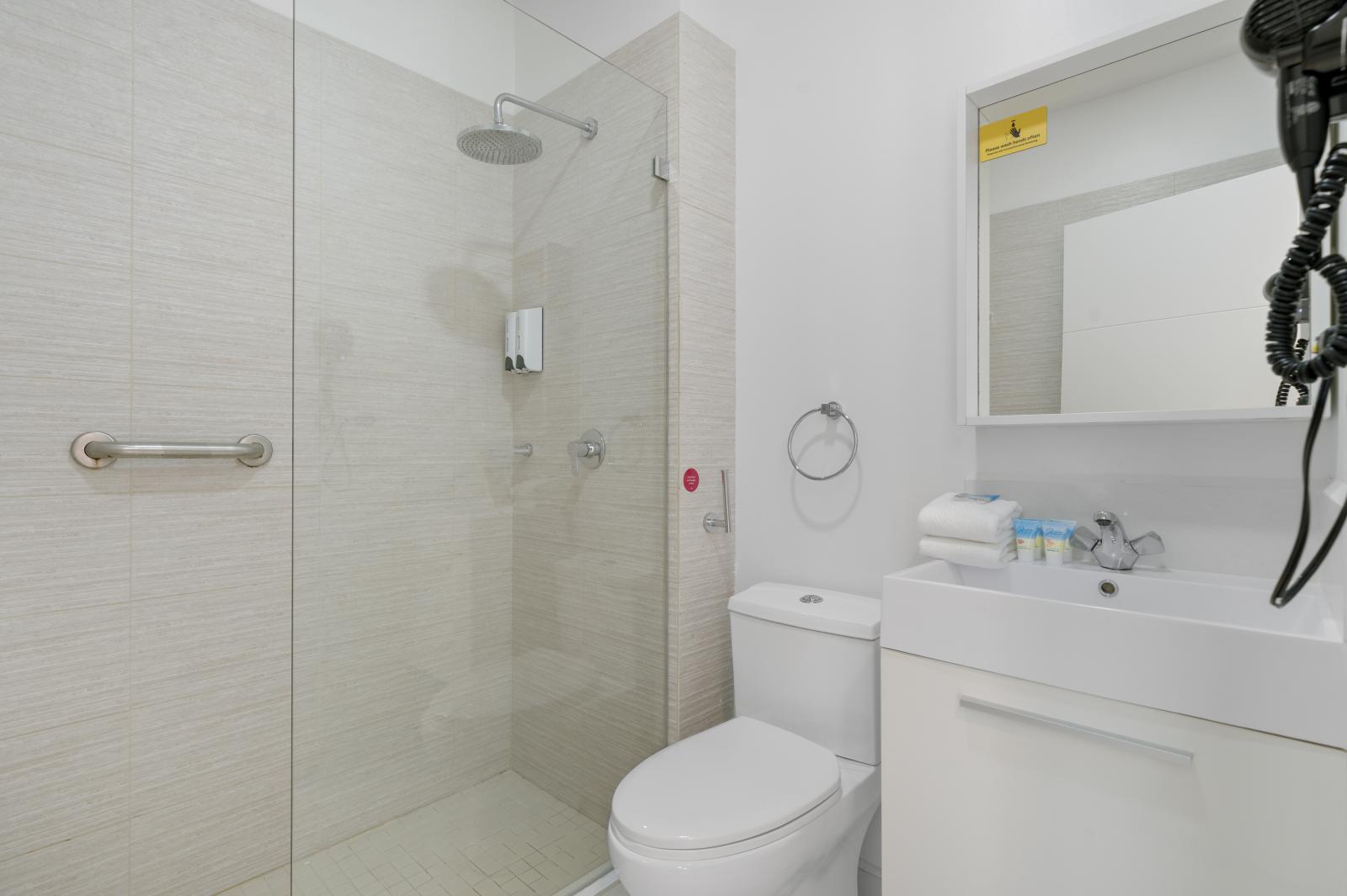 Modern bathroom with a sleek glass enclosed shower for a spa like experience - Clean, minimalist design with fresh towels & essential toiletries for a comfortable stay - Thoughtfully designed space with stylish accents, perfect for refreshing