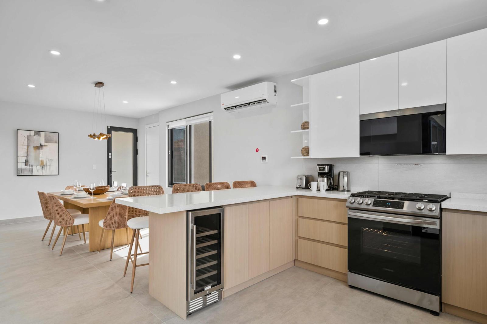 Open concept kitchen & dining area designed for effortless cooking & entertaining - Island with bar seating, wine cooler & modern appliances for a seamless stay - Enjoy meals together in a warm, inviting space just steps from the outdoor patio