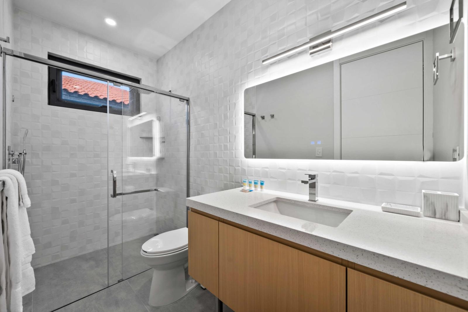 Spa like bathroom with a spacious walk in shower & glowing LED vanity mirror - Fresh towels & essential toiletries make your morning routine effortless & refreshing - Sleek, modern design ensures you feel pampered after a day of adventure in Aruba