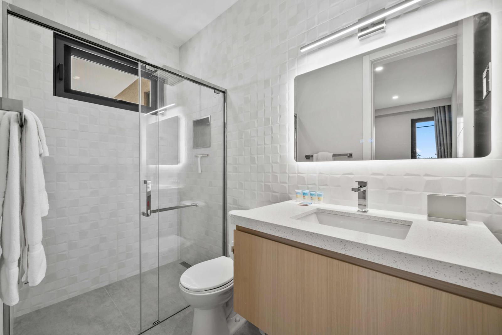 Sleek and modern bathroom with a glass-enclosed shower and soft LED lighting - Fresh towels, toiletries, and a spacious vanity make your morning routine effortless - Clean, bright, and refreshing space designed for total comfort during your stay