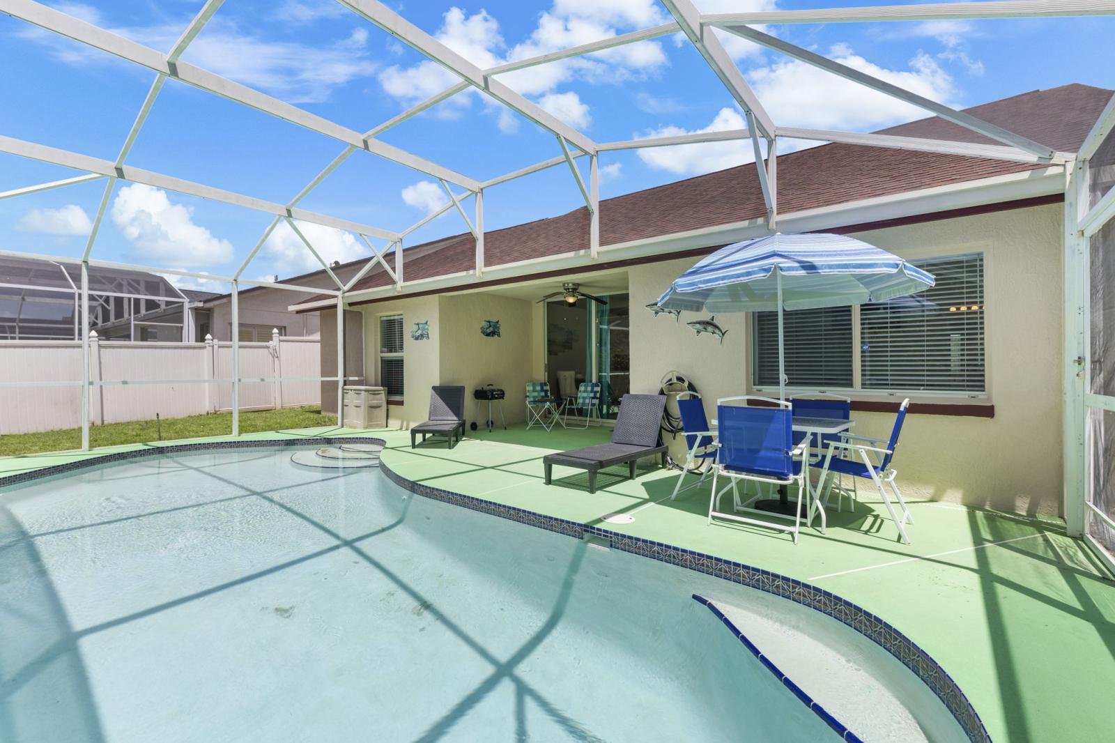 **Photo Caption:**  Covered lanai and screened-in pool area featuring sun loungers, outdoor dining set, and privacy fencing—perfect for relaxing or entertaining in the Florida sunshine.