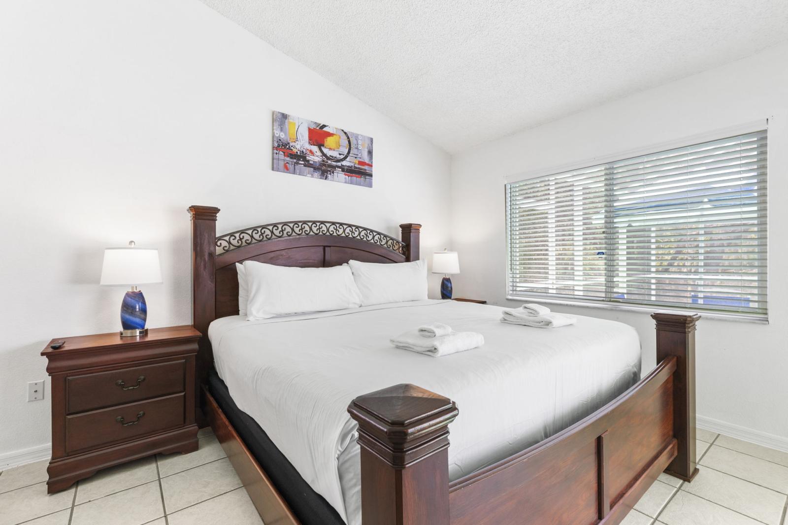 Spacious primary suite featuring a grand king bed, elegant wood furnishings, and abundant natural light pouring through large windows—your serene retreat after a day in the Florida sun.