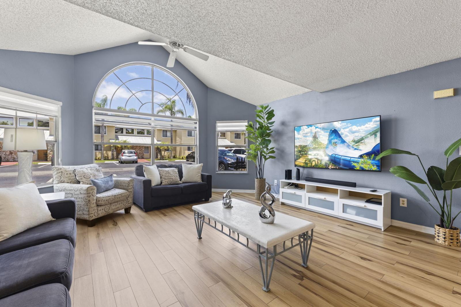 📺 Bright & Relaxing Lounge Space – Enjoy movie nights on the smart TV in this sun-filled living room with vaulted ceilings and large arched windows that bring the outdoors in. #SmartTV #NaturalLight #FamilyTime