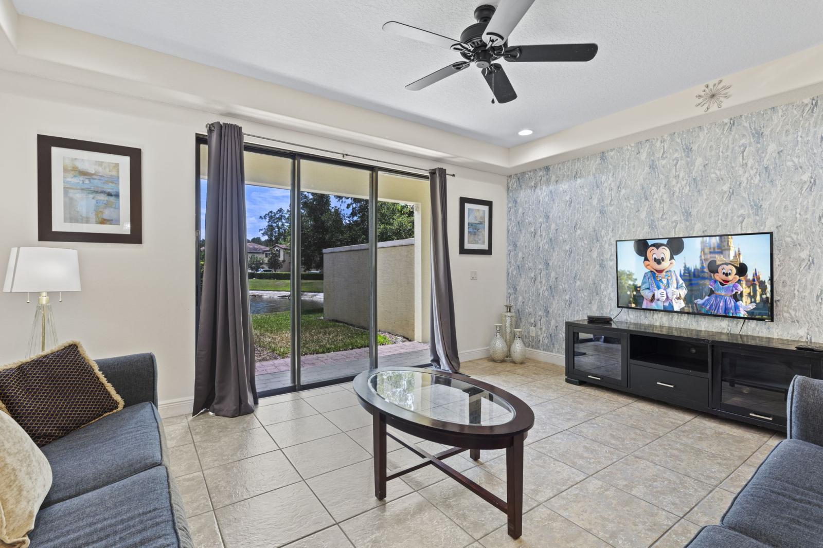 The entry opens to a bright, open-concept living room with a smart TV, a modern sitting area, and views of the lake through sliding doors that lead to the patio.