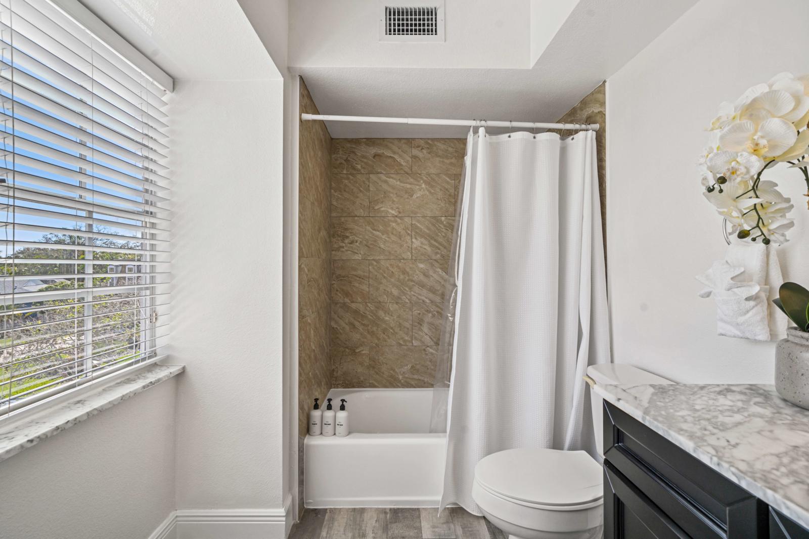 Spacious primary bathroom featuring a shower/tub combination, a modern toilet, and a generous vanity with ample counter space.
