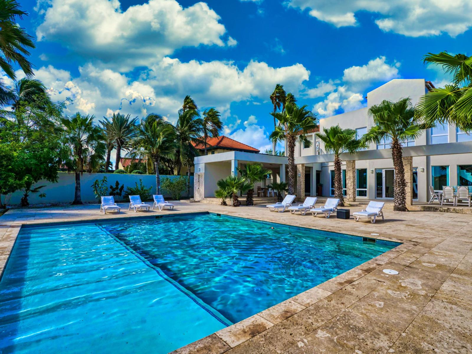 Luxury pool area of the villa in Noord, Aruba - Lush and refreshing environment - Cozy beach chairs available - Beautifully sunbathed space makes the soul peaceful - Experience the comfort at the best