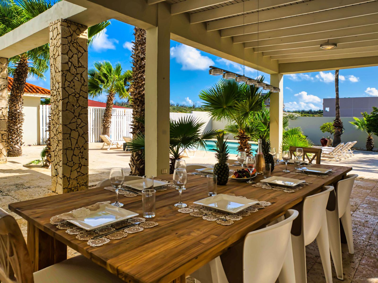 Relish in outdoor dining bliss at our covered dining table by the pool, offering a shaded retreat for enjoying meals amidst the refreshing ambiance of the poolside.