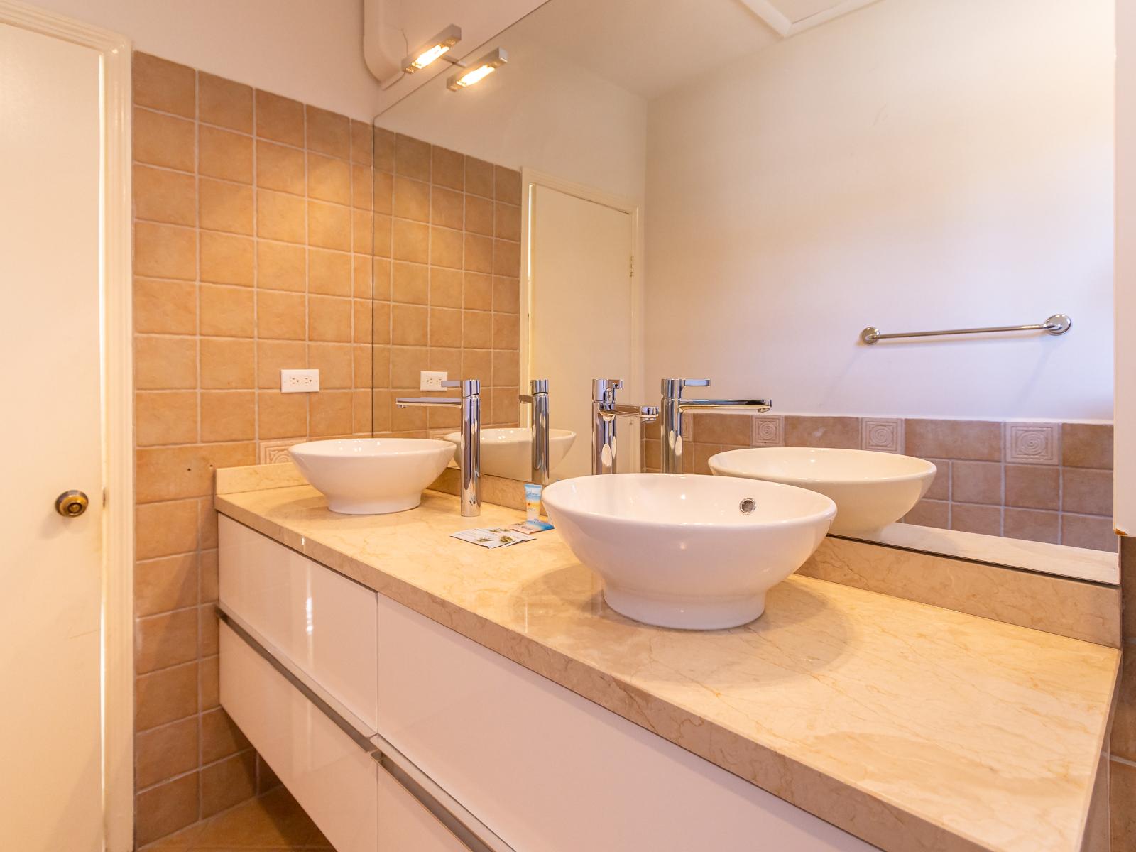 Polished Bathroom of the Villa in Aruba near Palm Beach - Elegant bathroom with luxurious fixtures and finishes - Double Vanity with full size Mirror - Chic design featuring a sleek vanity and upscale lighting - Walk-in Shower Area