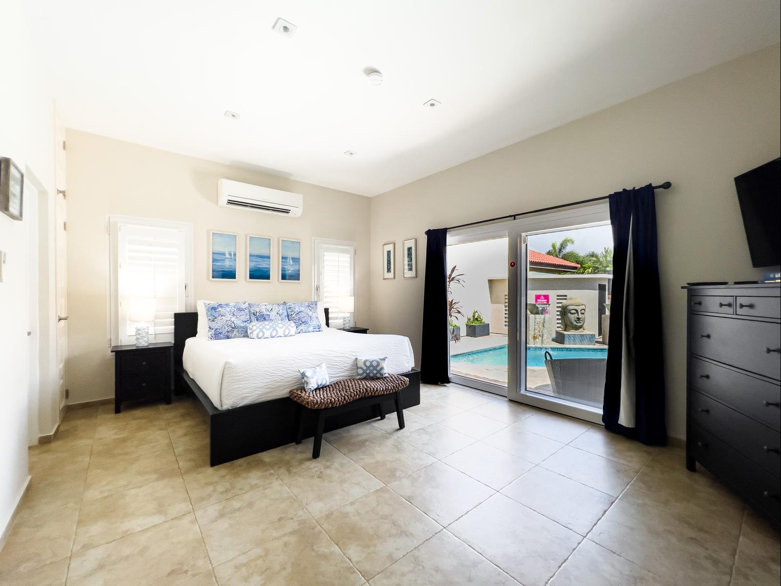 Lavish bedroom of the villa in Noord, Aruba - Comfy king size bed - Elegantly designed room beautifully decored with aesthetic wallpaper and paintings - Majestic table lamps - Large window mesmerizing with pool view - Availability of TV and Netflix