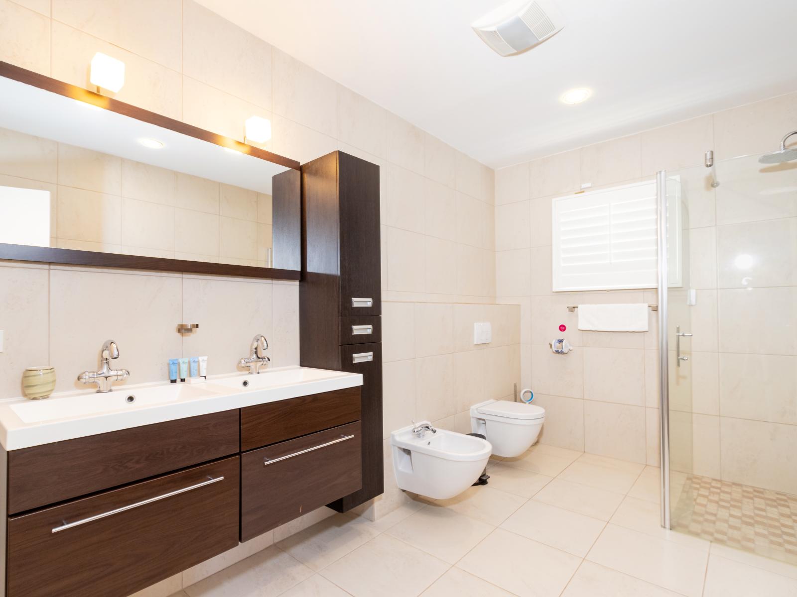 Polished Bathroom of the Villa in Noord Aruba - Seamless design featuring a glass-enclosed shower for a modern touch - Well-designed space with a focus on both aesthetics and functionality - Wooden Vanity with stylish look