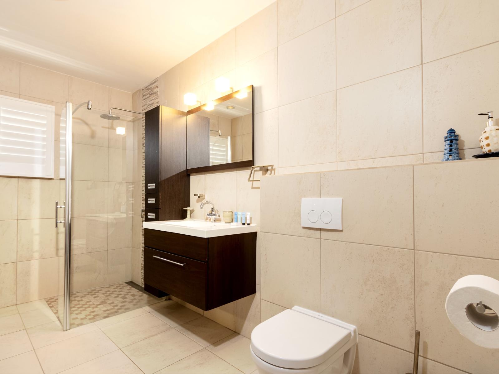 Polished Bathroom of the Villa in Noord Aruba - Chic design featuring a sleek vanity and upscale lighting - Seamless design featuring a glass-enclosed shower - Spacious layout offering a sense of luxury and comfort