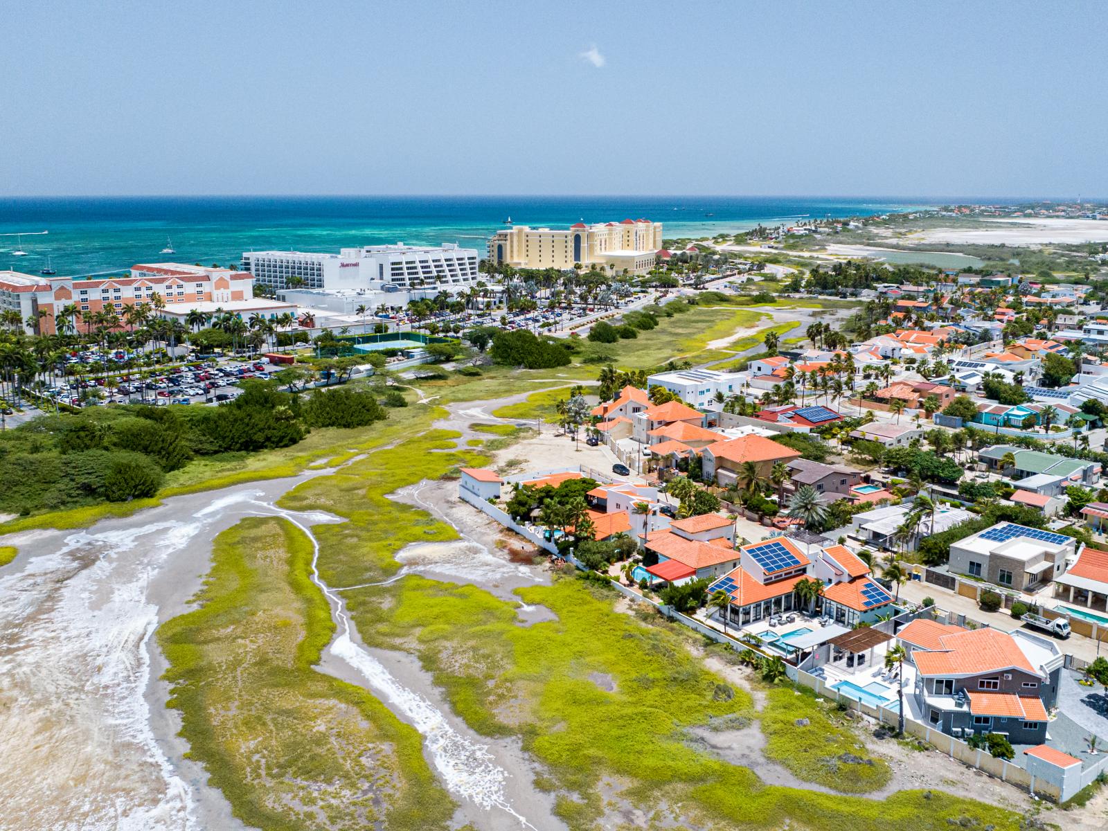 Captivating Neighborhood Panorama: Behold the mesmerizing blend of the neighborhood's vibrant energy, scenic Hooiberg, serene saliña, and the majestic high-rise area, including the iconic Marriott hotels, all captured in this stunning aerial shot.